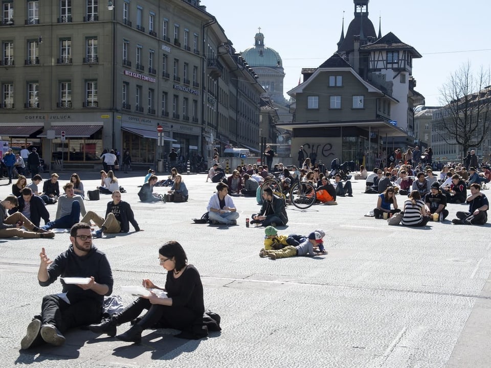 Menschen auf grossem Platz bei Sonnenschein sitzend.