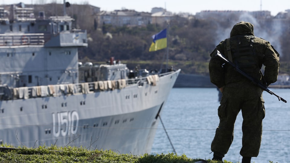 Ein Soldat steht beim Hafen mit Blick auf ein Kriegsschiff.