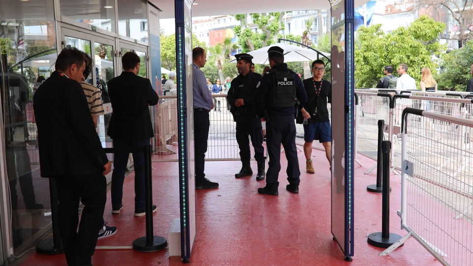 Sicherheitskontrolle mit Tor (wie bei Flughafen), im Hintergrund Polizei.