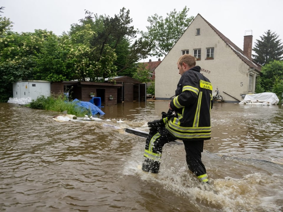 Feuerwehrmann watet durch Hochwasser vor einem überfluteten Gebäude.