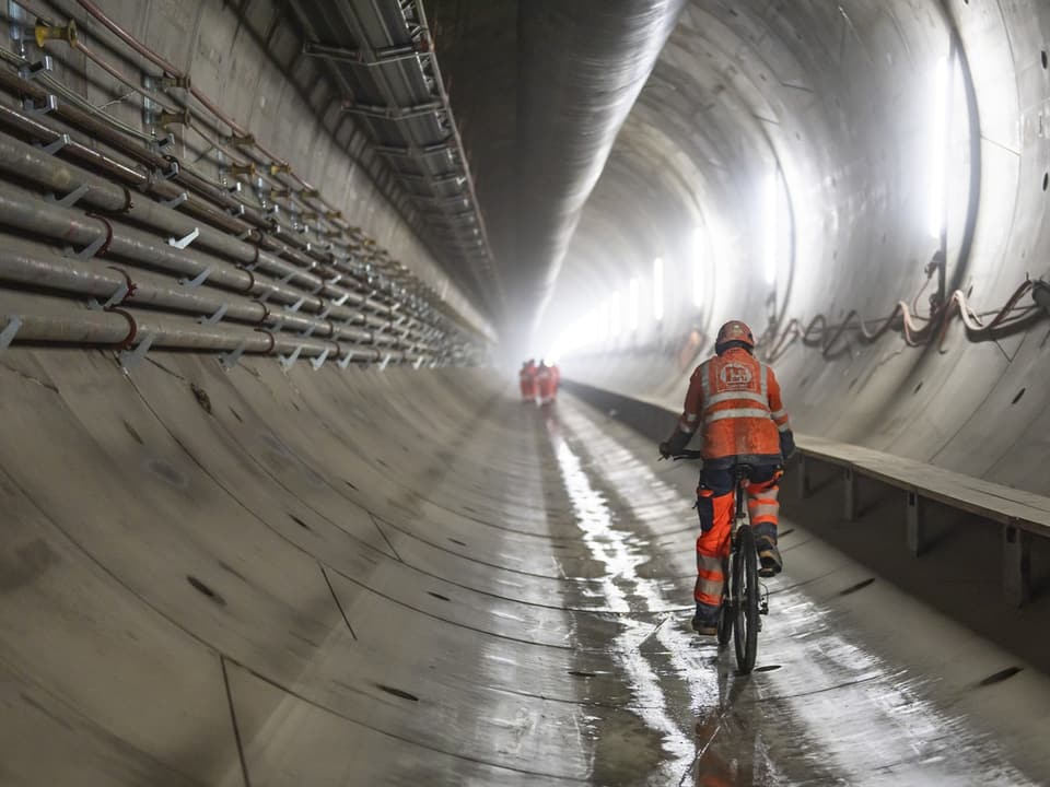 Arbeiter in Bauweste fährt Fahrrad durch Tunnel.