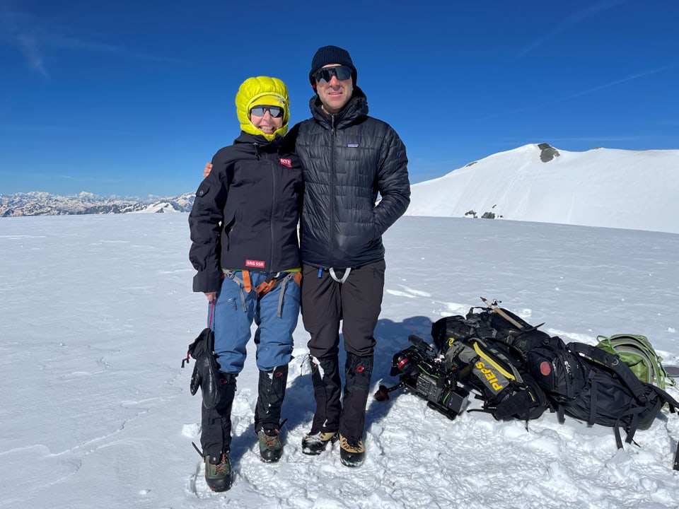 Zwei Personen in Winterkleidung auf einem verschneiten Berggipfel.