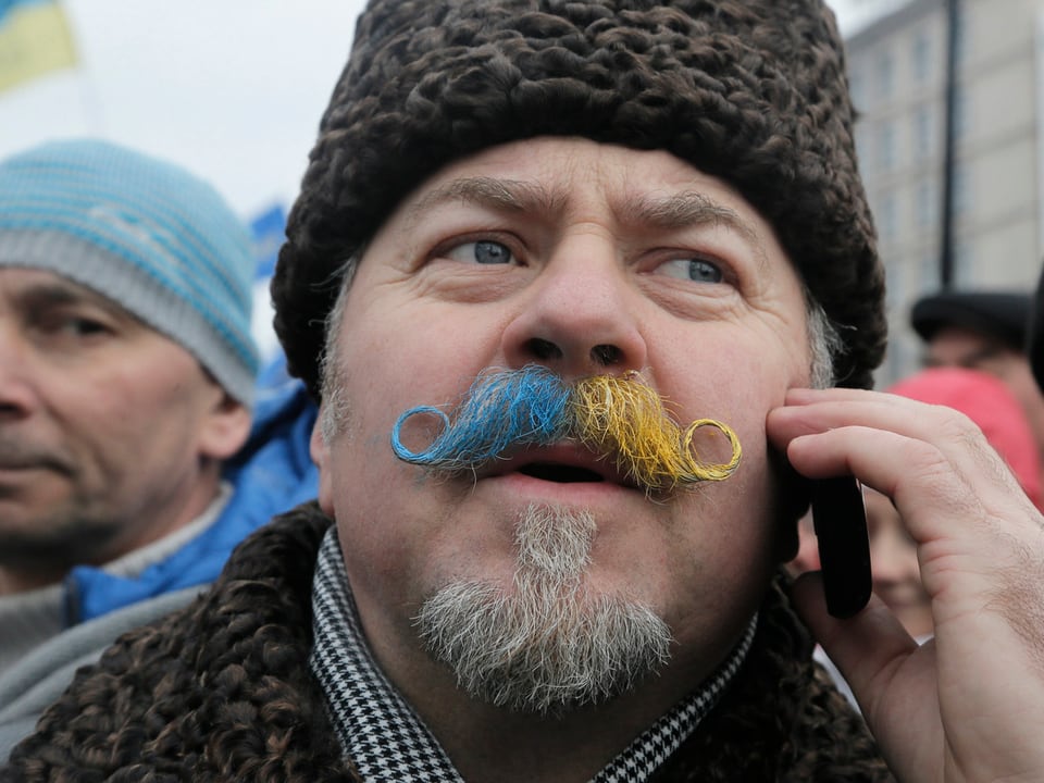 Ein Ukrainer mit Schnauz in den Nationalfarben spricht am Handy.