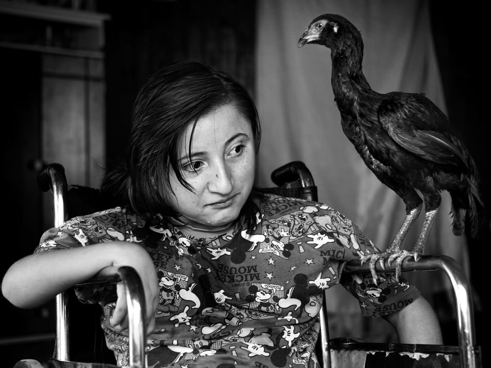 Ein Mädchen im Rollstuhl, auf dessen linker Armlehne ein schwarzer Vogel sitzt.
