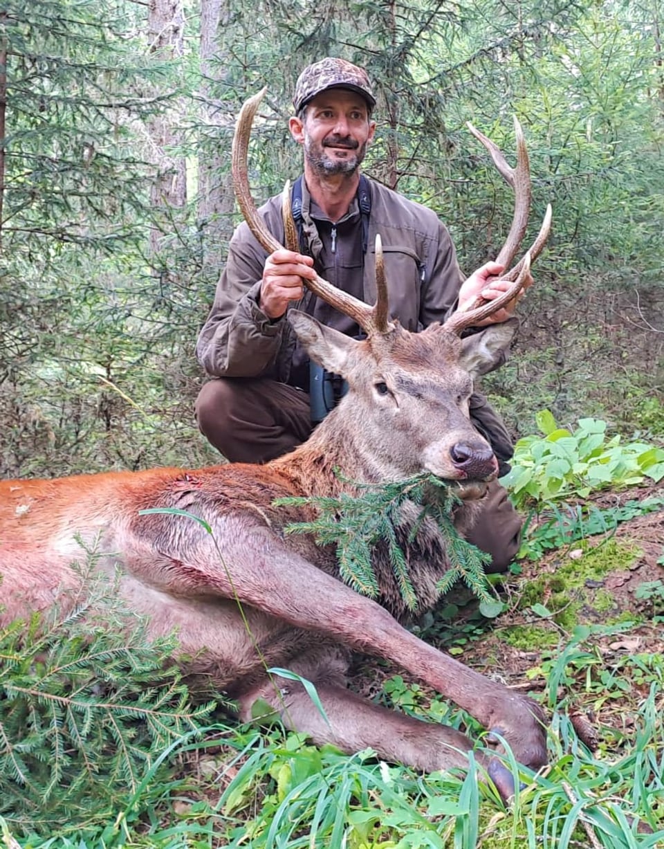 Mann posiert mit erlegtem Hirsch im Wald.