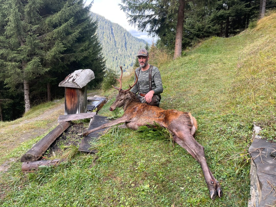 Mann posiert mit erlegtem Hirsch im Wald.