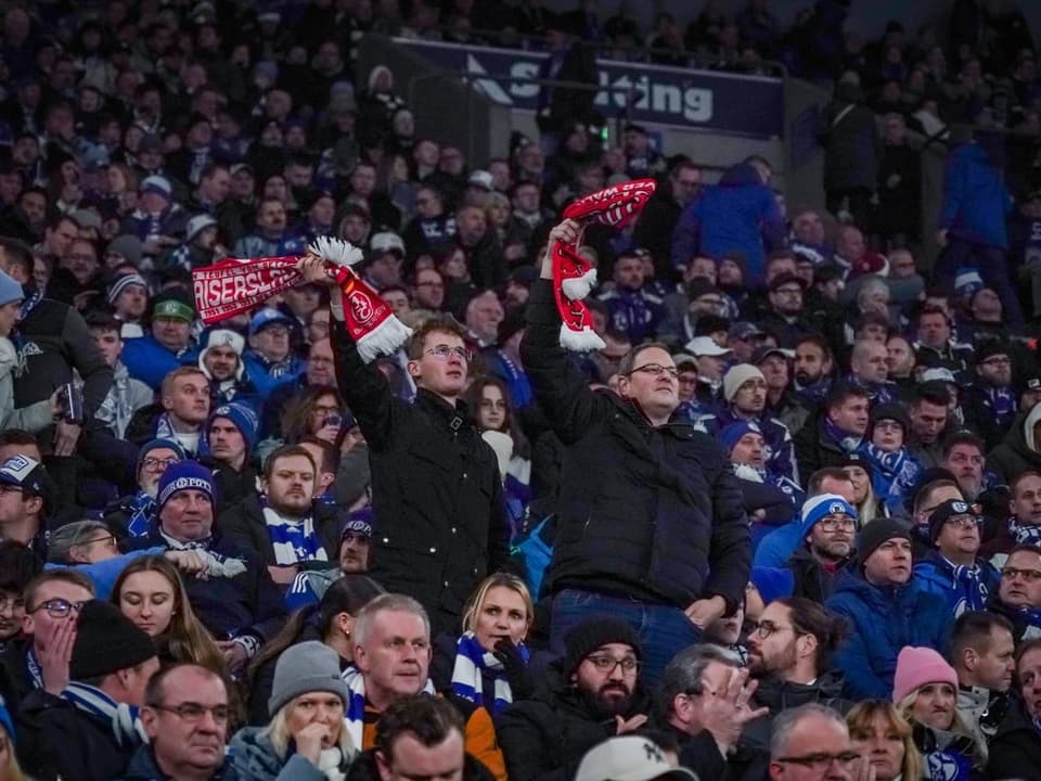 Fussballfans jubeln mit Schals im Stadion.