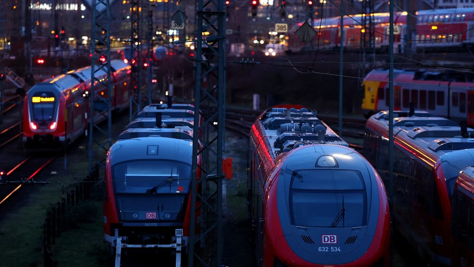 mehrere Züge im Dunkeln, stehen auf Gleisen. Dahinter verschwommen eine Bahnhofshalle.