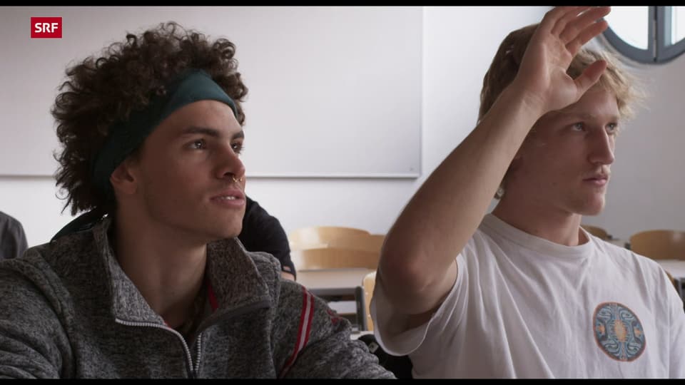 Junger Mann mit Locken und Stirnband im Klassenzimmer.