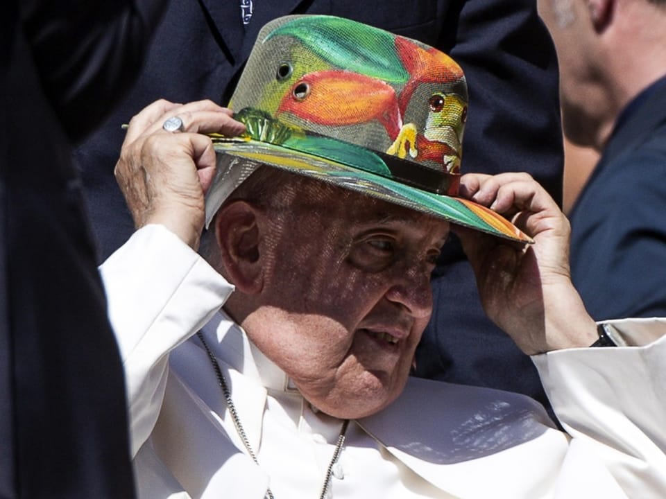 Papst Franziskus setzt sich einen farbigen Hut auf.