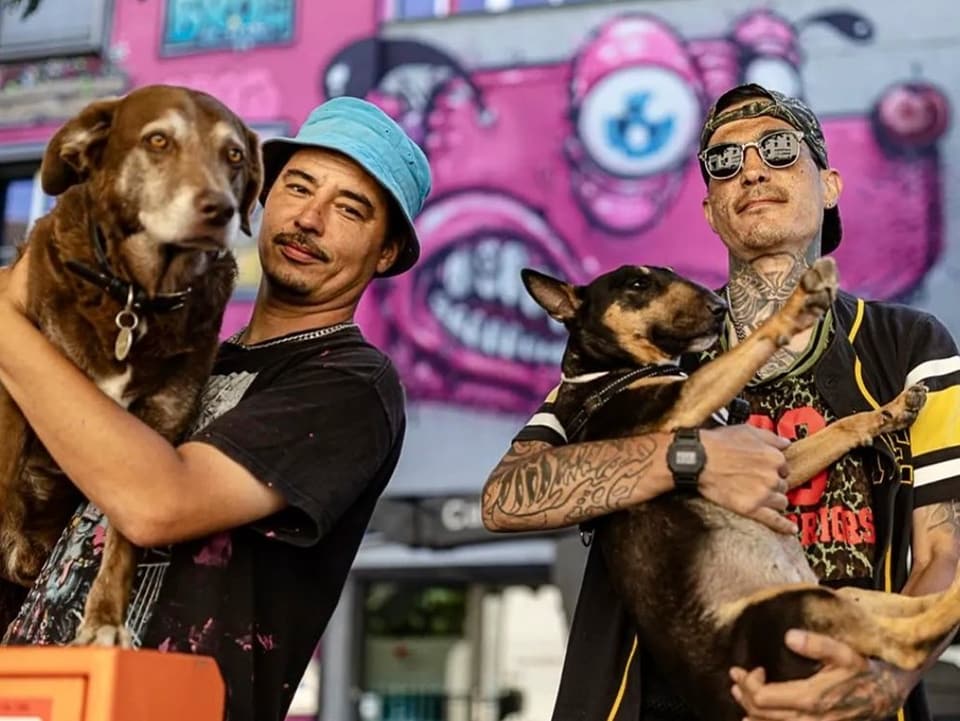 Die Brüder stehen mit ihren Hunden vor einer Fassade mit rosarotem Hundegraffiti