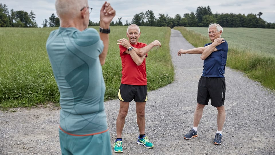 Drei ältere Luzerner Männer in Jogging-Anzügen stretchen ihre Arme.