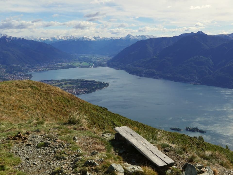 Holzbank auf einem Hügel mit Blick auf einen See und Berge.