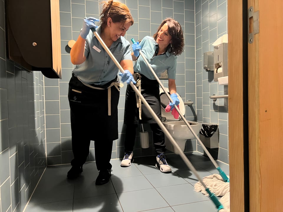 Mona und Sarra putzen den Boden der Toilette mit Mopps.