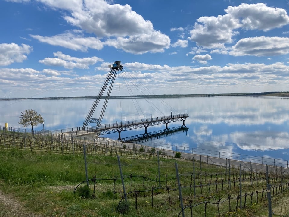 Aussichtsplattform über See mit Wolken und Wiesen im Vordergrund.