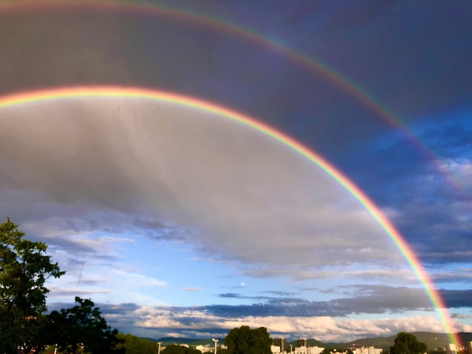 Doppelter Regenbogen am Himmel über Stadt und Natur.
