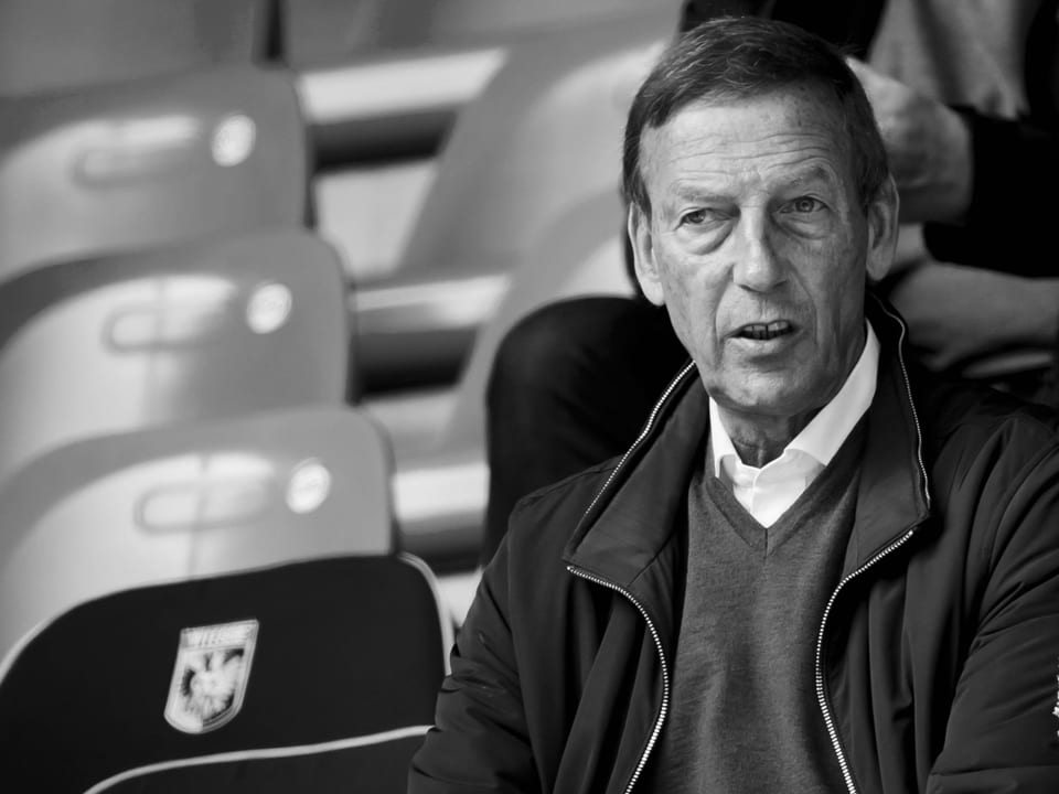 Älterer Mann sitzt auf Stadiontribüne.