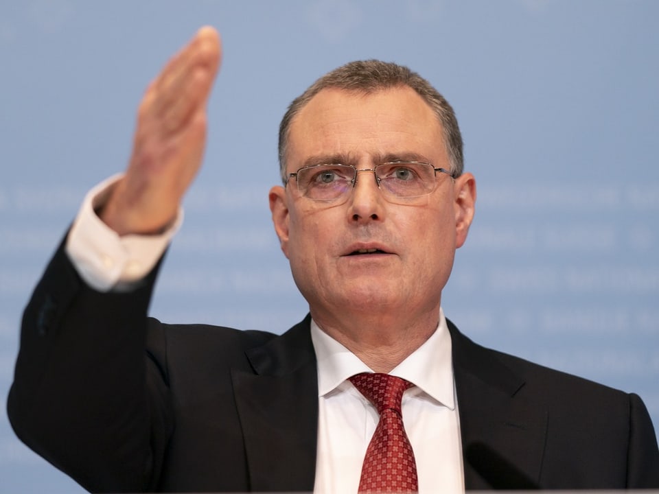 Mann in Anzug hebt Hand in gestikulierender Pose.