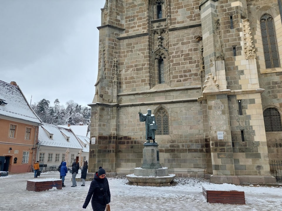 Verschneiter Platz vor einer gotischen Kirche mit Statue.