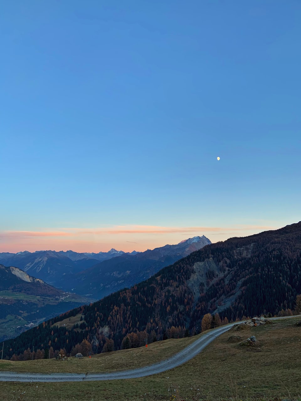 Berglandschaft bei Sonnenuntergang mit Mond am Himmel.