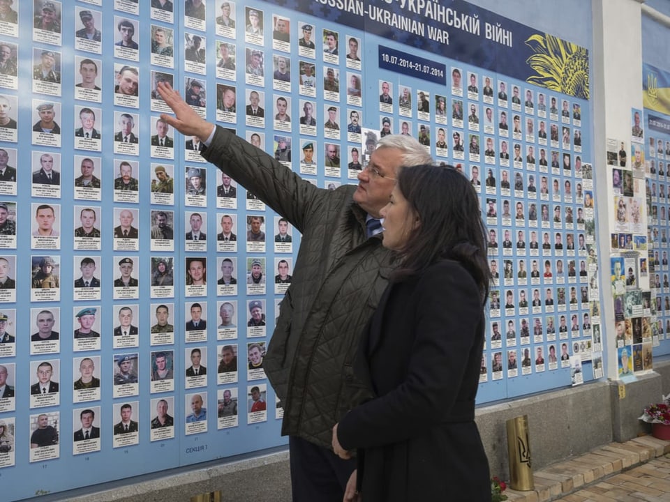 Baerbock und Sybiha betrachten Wand mit Porträtfotos gefallener Soldaten.