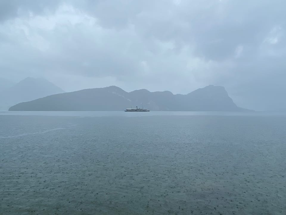 Schiff auf einem nebligen See mit Bergen im Hintergrund.