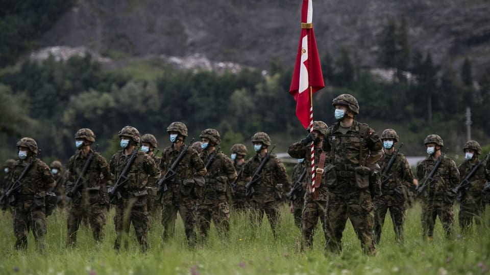 Soldaten (mit Gesichtsmaske) stehen in einem Feld, einer hält eine Schweizer Fahne.