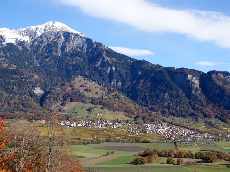 Landschaftsbild mit Blick auf ein Dorf vor einer Bergkette.