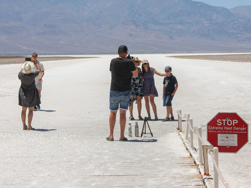 Personen posieren für Fotos in einer trockenen Landschaft mit einem Warnschild für extreme Hitze.