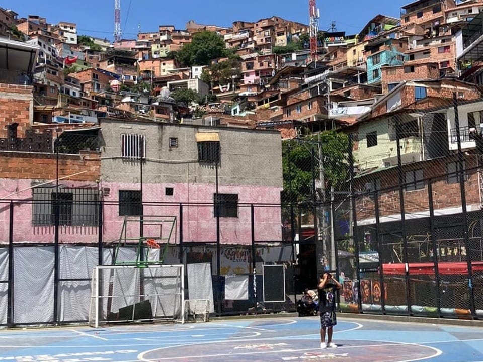 Boy on basketball court in front of mountain with favela houses.
