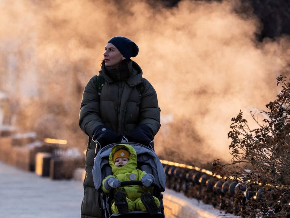 Frau schiebt Kinderwagen im Winter.