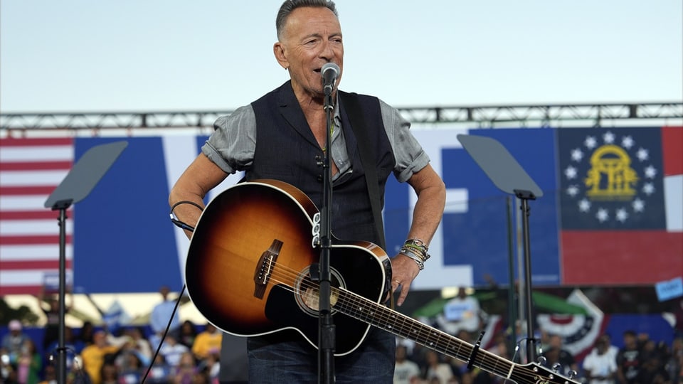 Springsteen spricht mit umschlungener Gitarre zum Publikum.