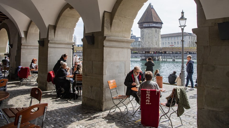 Menschen sitzen in Luzern an der Reuss in einem Restaurant.