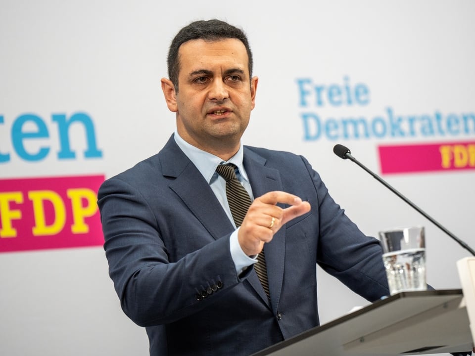 Mann hält Rede mit FDP-Logo im Hintergrund.