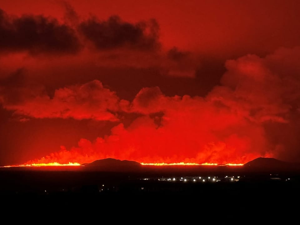 Lavaeruption unter rotem Himmel in der Nacht.