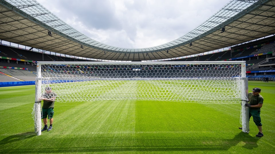 Zwei Arbeiter stellen ein Fussballtor in einem leeren Stadion auf.