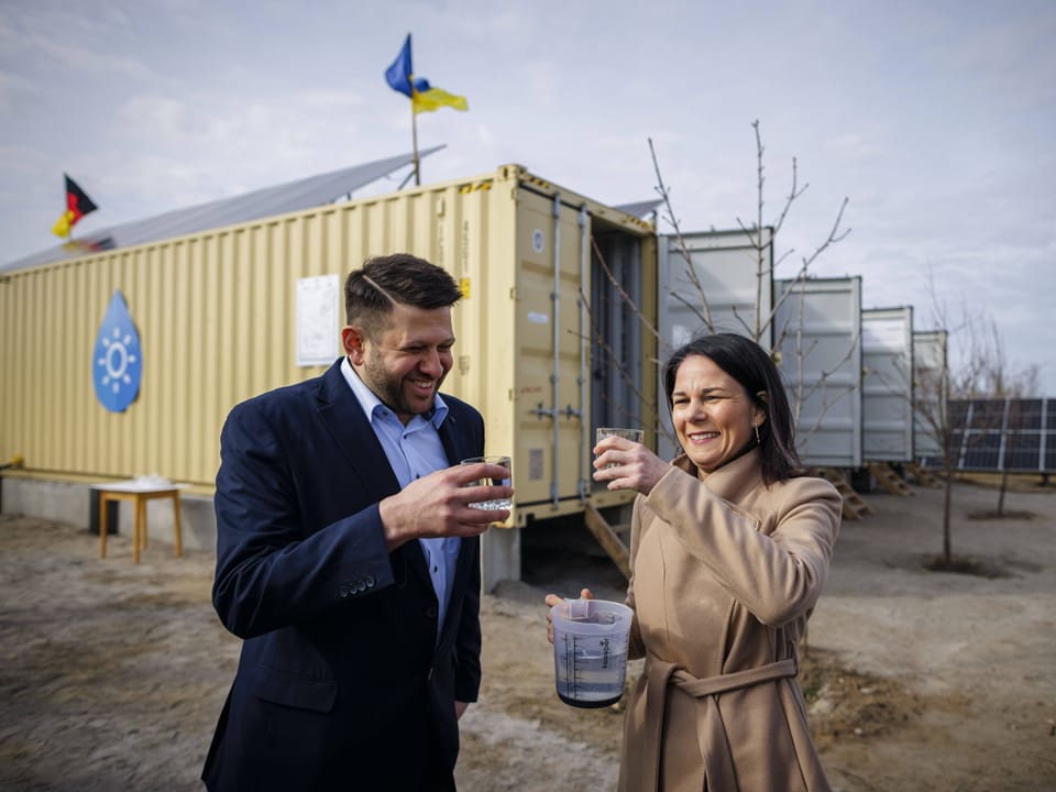 Mann und Frau trinken Wasser vor einem Container mit Wassertropfen-Symbol.