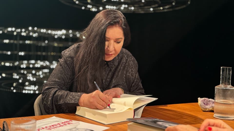 Marina Abramovic sitzend, die Bücher signierend.