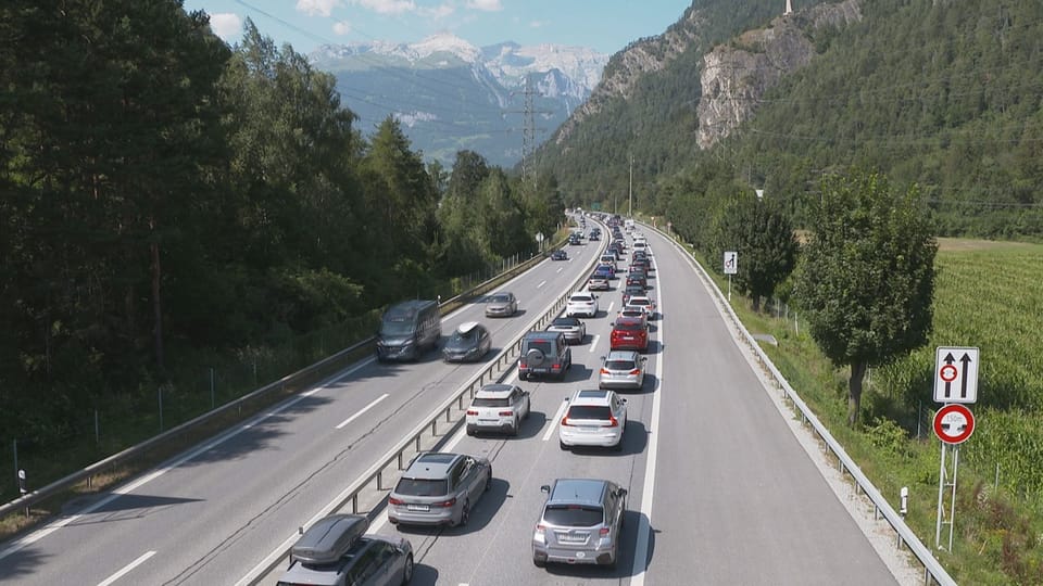 Stau auf der zweispurigen Autobahn A13 in bergiger Landschaft.