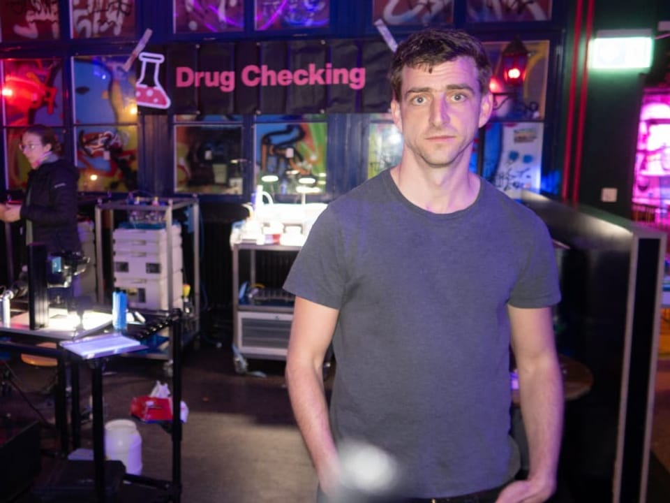 Mann in einem Raum mit 'Drug Checking' Schild im Hintergrund.