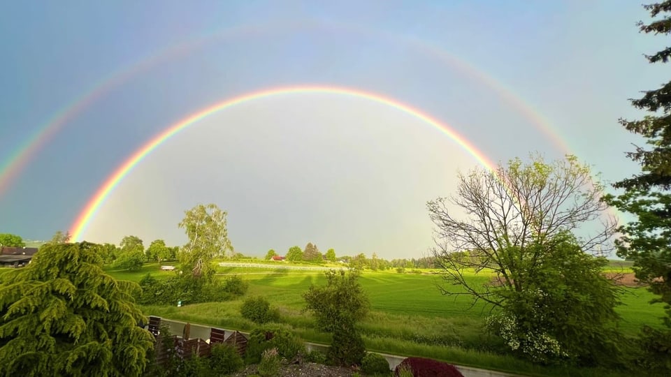 Doppelter Regenbogen über einer grünen Landschaft.