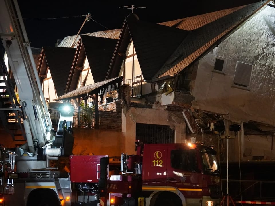 Feuerwehrfahrzeug neben beschädigten Gebäuden bei Nacht.