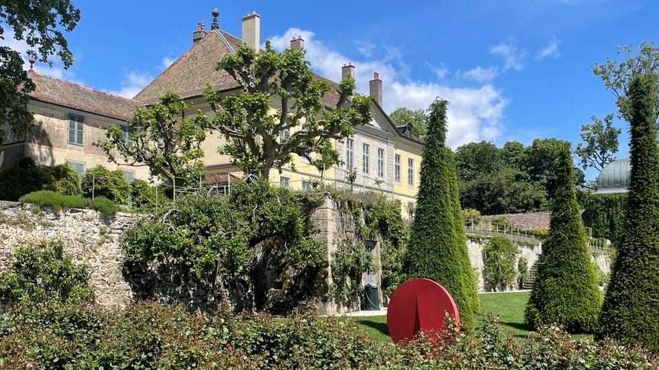 Schloss mit Garten, viel Grün und ein rotes Kunstwerk