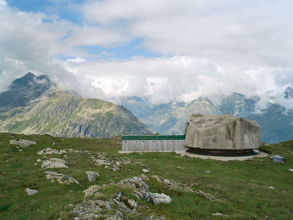 Steinobjekt in alpiner Berglandschaft mit Wolken.