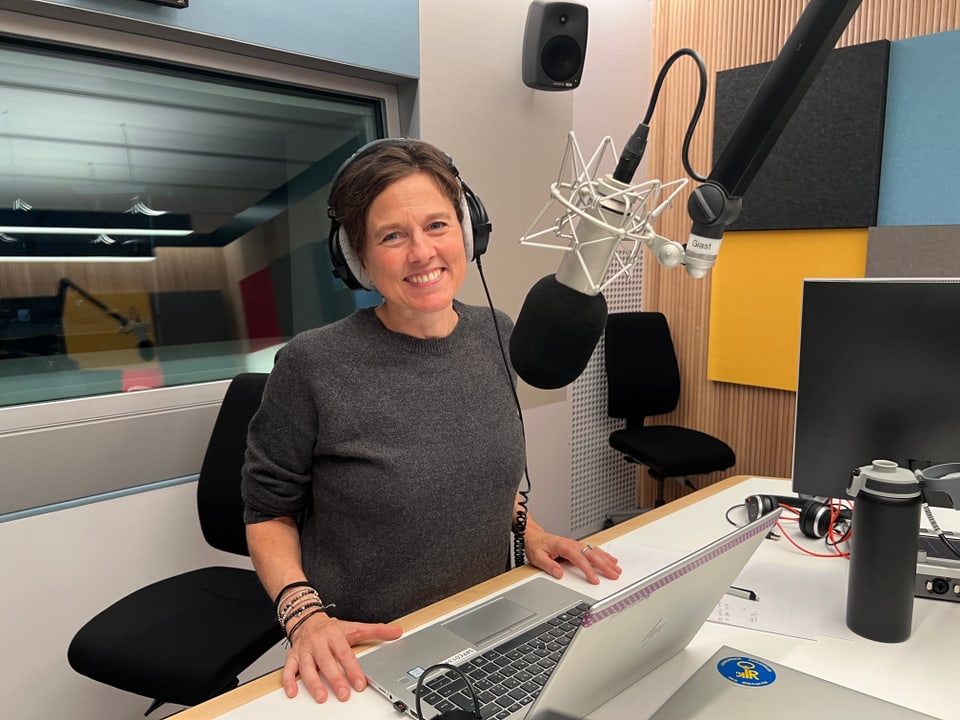 Frau mit Kopfhörern im Tonstudio vor Mikrofon und Laptop.