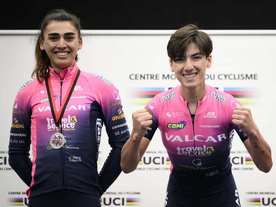 Zwei Radrennfahrer in rosa Trikots mit Medaille im UCI-Zentrum.