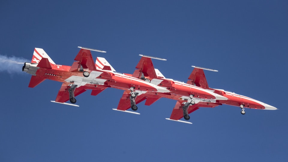 Drei rote Kunstflugzeuge in Formation am blauen Himmel.