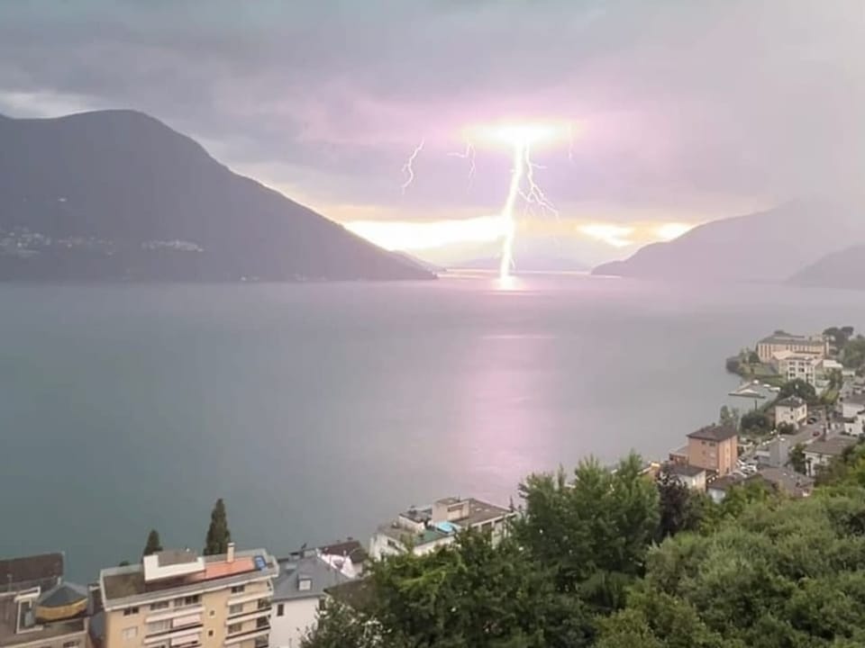 Blitz über einem Bergsee neben einer Stadt.