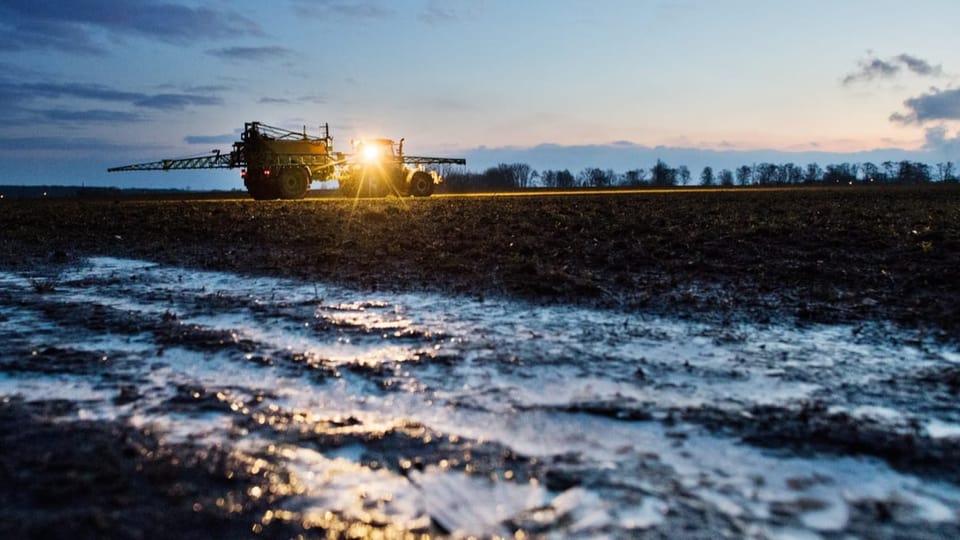 Traktor düngt beim Sonnenuntergang ein Feld