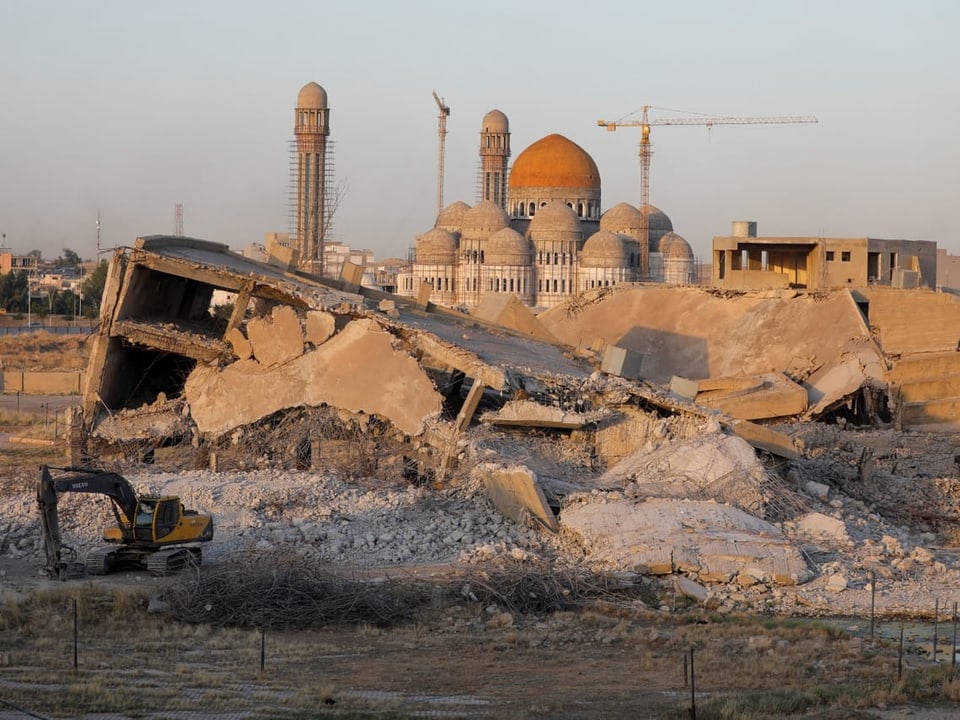 Blick auf zerstörte Gebäude und eine Moschee mit Kuppeln und Minaretten im Hintergrund.